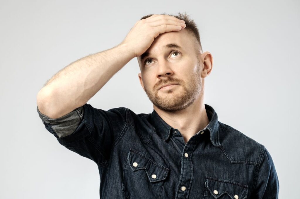 Homem com cabelo ralo com mão na testa cobrindo entradas.