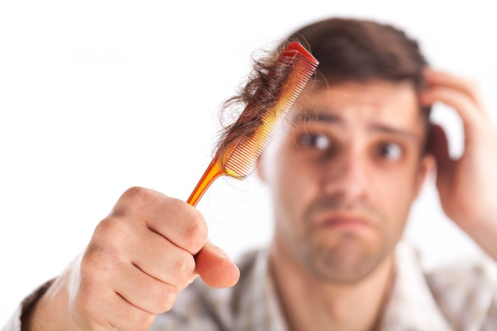 Homem olhando preocupado segurando pente com muitos fios de cabelo.