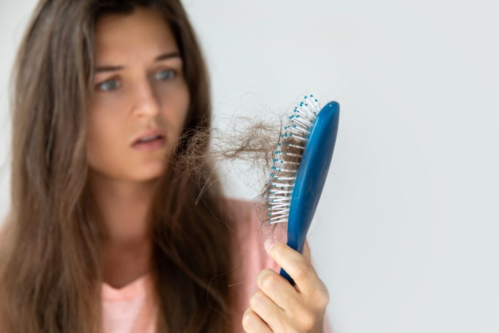 mulher olhando para a escova cheia de cabelo, pensando no que pode causar queda de cabelo