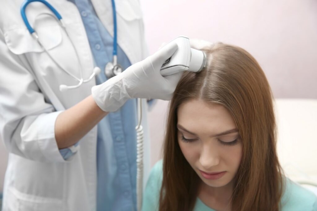 Médico especialista em queda de cabelo feminino: quando procurar e como tratar o problema? um médico especialista em queda de cabelo feminino examinando o couro cabeludo de uma paciente com o auxílio de um dermatoscópio. .