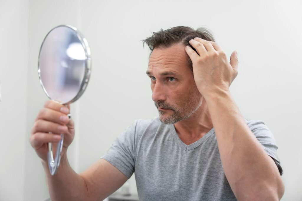 Homem observando o couro cabeludo no espelho após usar produto para queda de cabelo.